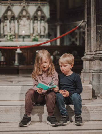 To barn, en jente og en gutt sitter i trappen foran alteret i Nidarosdomen og leser i et grønt aktivitetshefte.