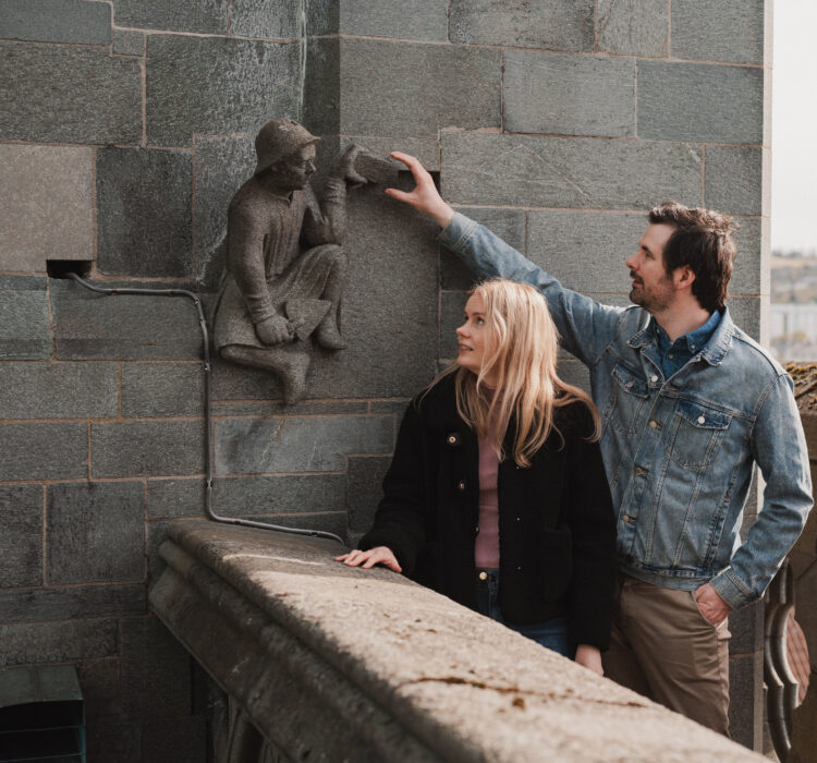 Kvinne og mann står oppe på vestfronten å ser på en statue av en murer